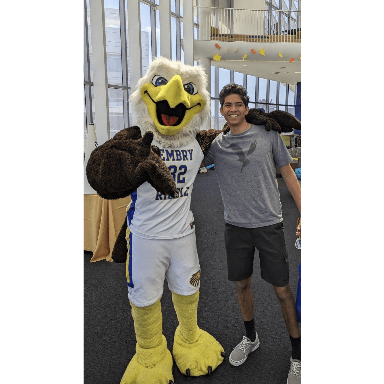 Adam, in shorts and a eagle t-shirt, stands next to the eagle mascot, who wears a basketball uniform.