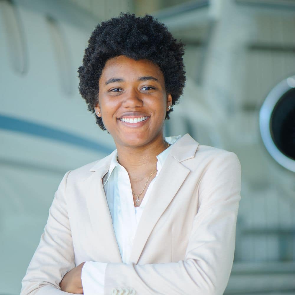 Sydney Jones, MBA student and member of the Daytona Beach Campus Student Government Association & National Society of Black Engineers. smiles while standing in front of an aircraft