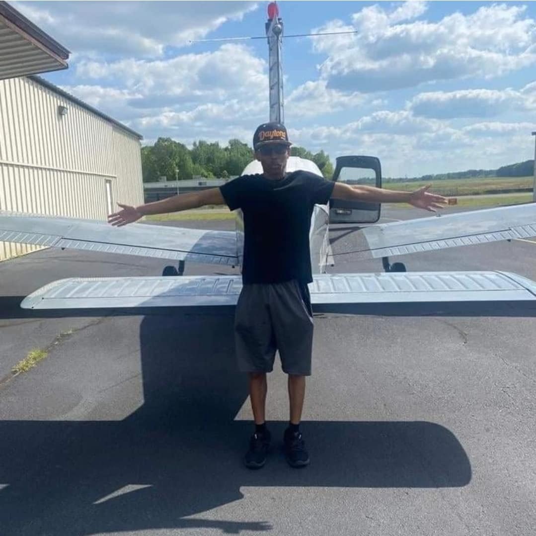 Dressed casually, Josiah poses behind a small plane near a hangar.
