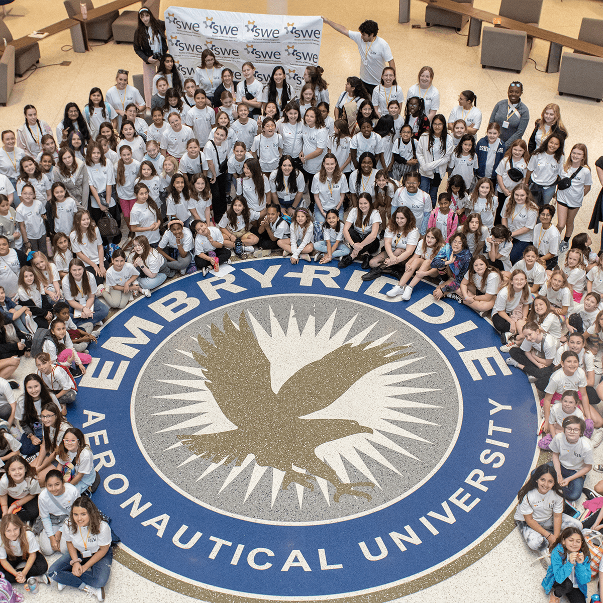 Young girls from Volusia County pose around the Embry-Riddle seal in the Mori Hosseini Student Union during the Introduce a Girl to Engineering Workshop (IGEW) led by the Society of Women Engineers (SWE) Collegiate Section at the Daytona Beach campus on Feb. 17, 2024. (Photo: Embry-Riddle)