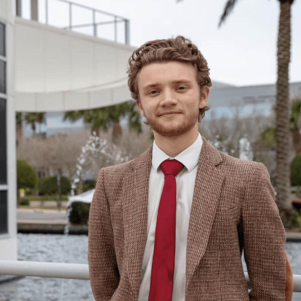 A person wearing a suit and tie, standing outside.