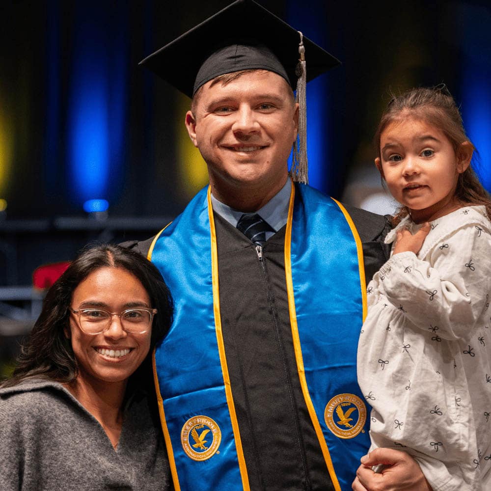 A person wearing graduation regalia, standing with their family.