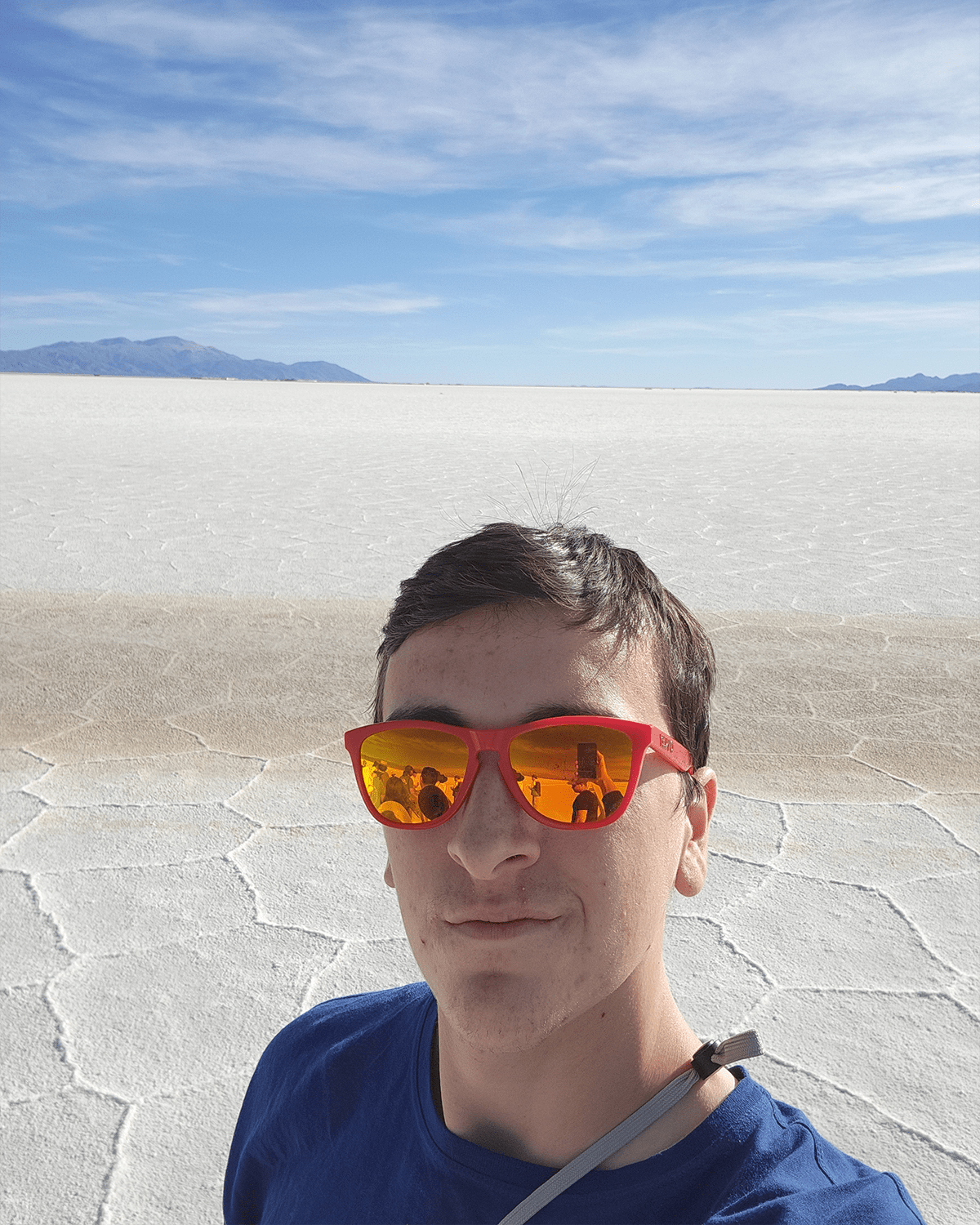 Zackrey poses wearing bright orange sunglasses in front of an empty expanse of dry, cracked earth.