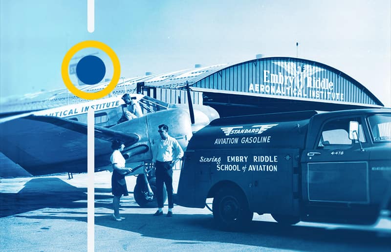A blue-toned black and white photograph of a 1950s-era gasoline truck is shown fueling a prop plane in front of a hangar with the Embry-Riddle eagle logo over the door.