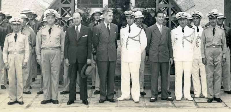 A group of officers, instructors and cadets. From Left to Right: Lt. Col. Ribeiro, Director of Training; Col. H. D. Fontenelle, Commanding Officer of Afonsos Field, Brazilian Air Force Academy; Brazilian Air Minister, Dr. J. P. Salgado Filho; Mr. John Paul Riddle, President of Embry-Riddle Co.; Major Farias Lima, aide to the Minister, Mr. Adriano Ponso, technical assistant to Mr. Riddle; Col. Adil Oliveira, General Staff; Captain Luis Sampaio, aide to the Minister; and two officers of the School. Afonsos Field, Rio de Janeiro.