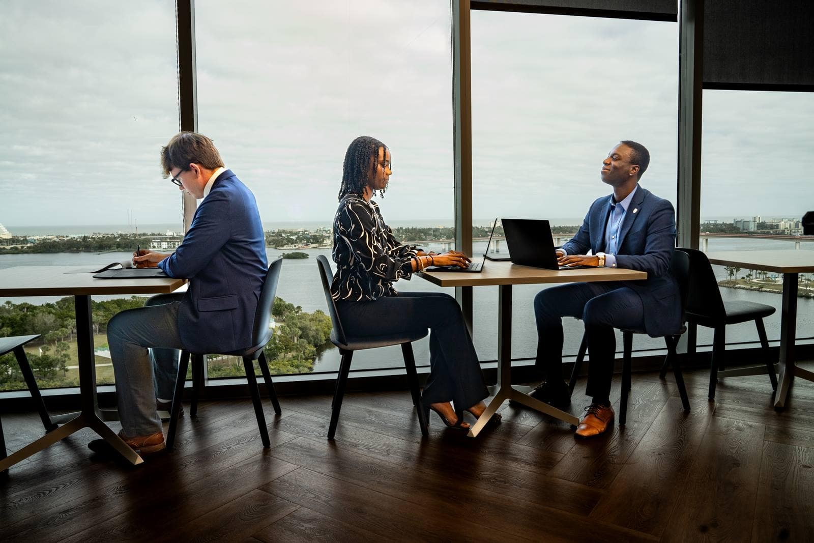 Three people sitting at tables with a view of a lake. 