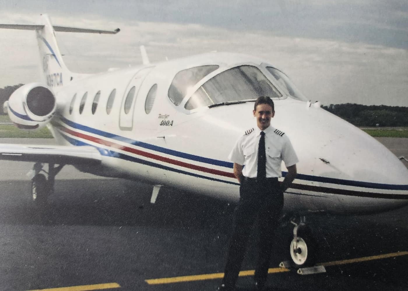 Chase, in a pilot's uniform, poses in front of a small jet.