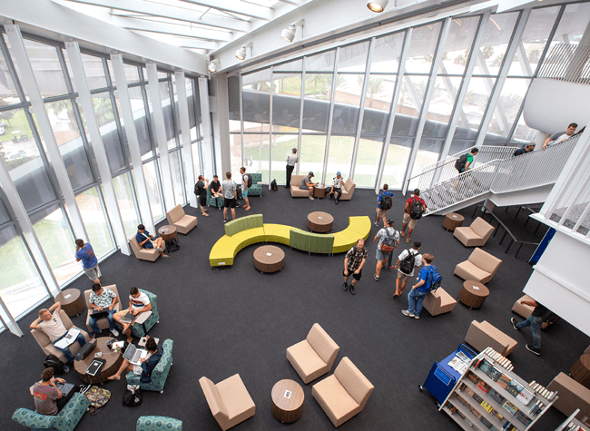 Seen from above, students meet and study in Hunt Library common space, in front of two walls of floor to ceiling windows.