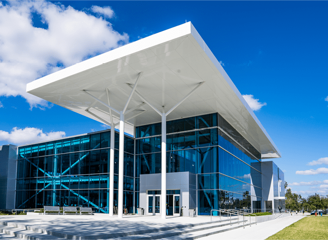 The Eagle Fitness Center, a reflective glass building with a white canopy two stories above the entrance.