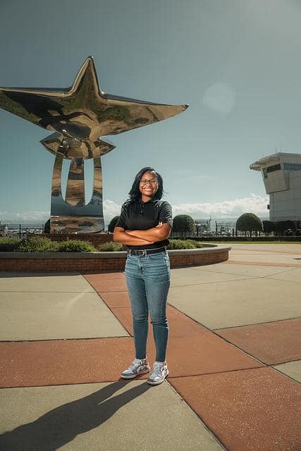 Olivia Munisi stands confidently in front of the silver plane/bird sculpture on the Daytona Beach Campus, Pathways to the Sky.
