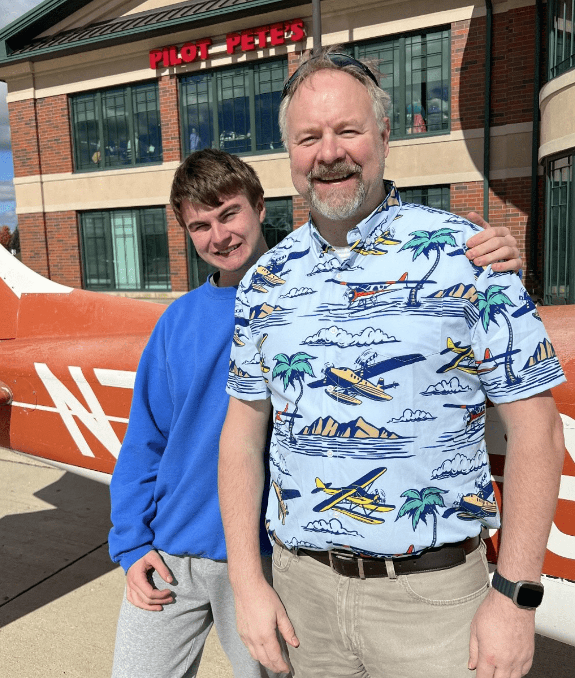 Killian poses with his arm around his father, in front of an orange aircraft.