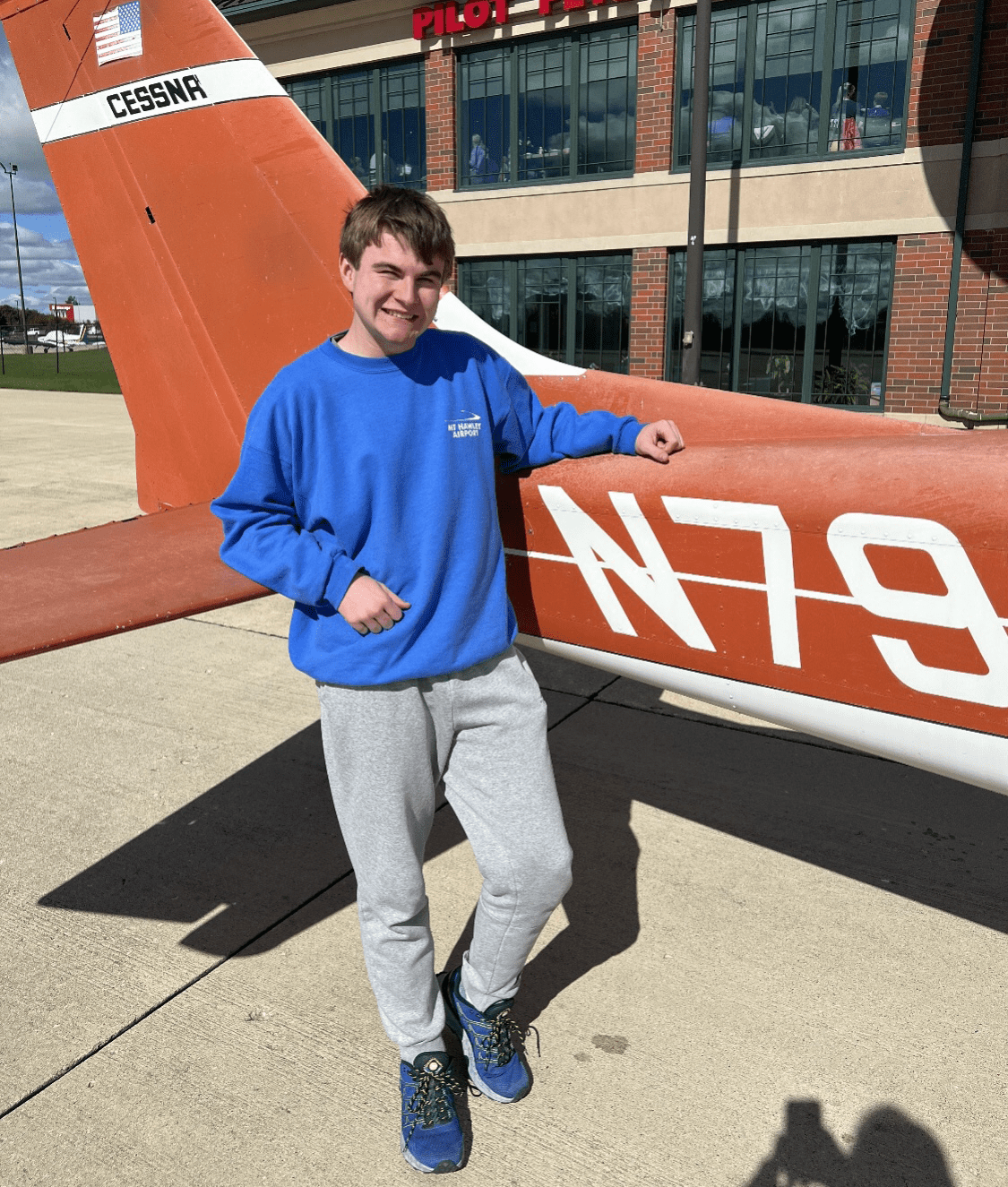 Killian, wearing a blue sweatshirt, poses in front of an orange Cessna.