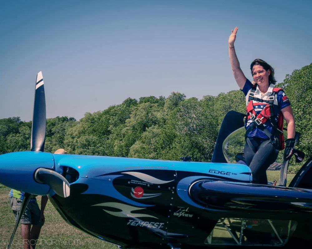 Melissa Burns, smiling and waving in a blue plane.