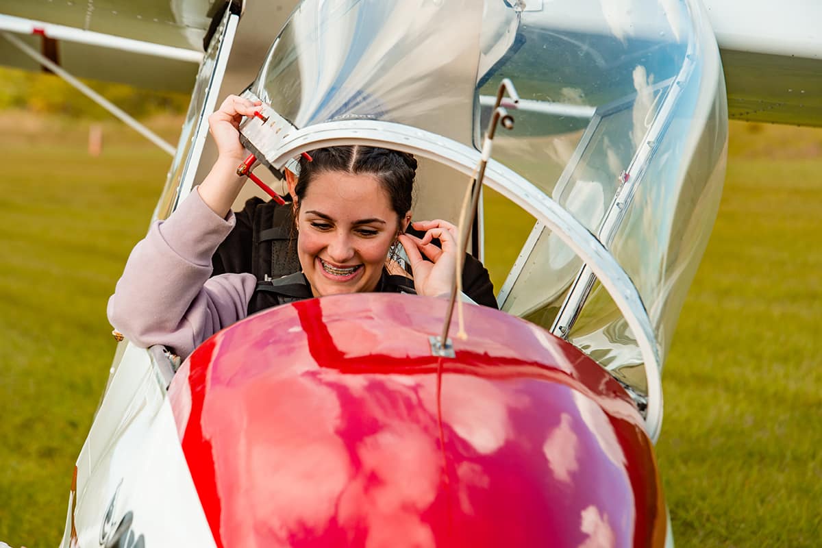 Ava pulls the windshield of a small plane down over her as she's seated in the cockpit.