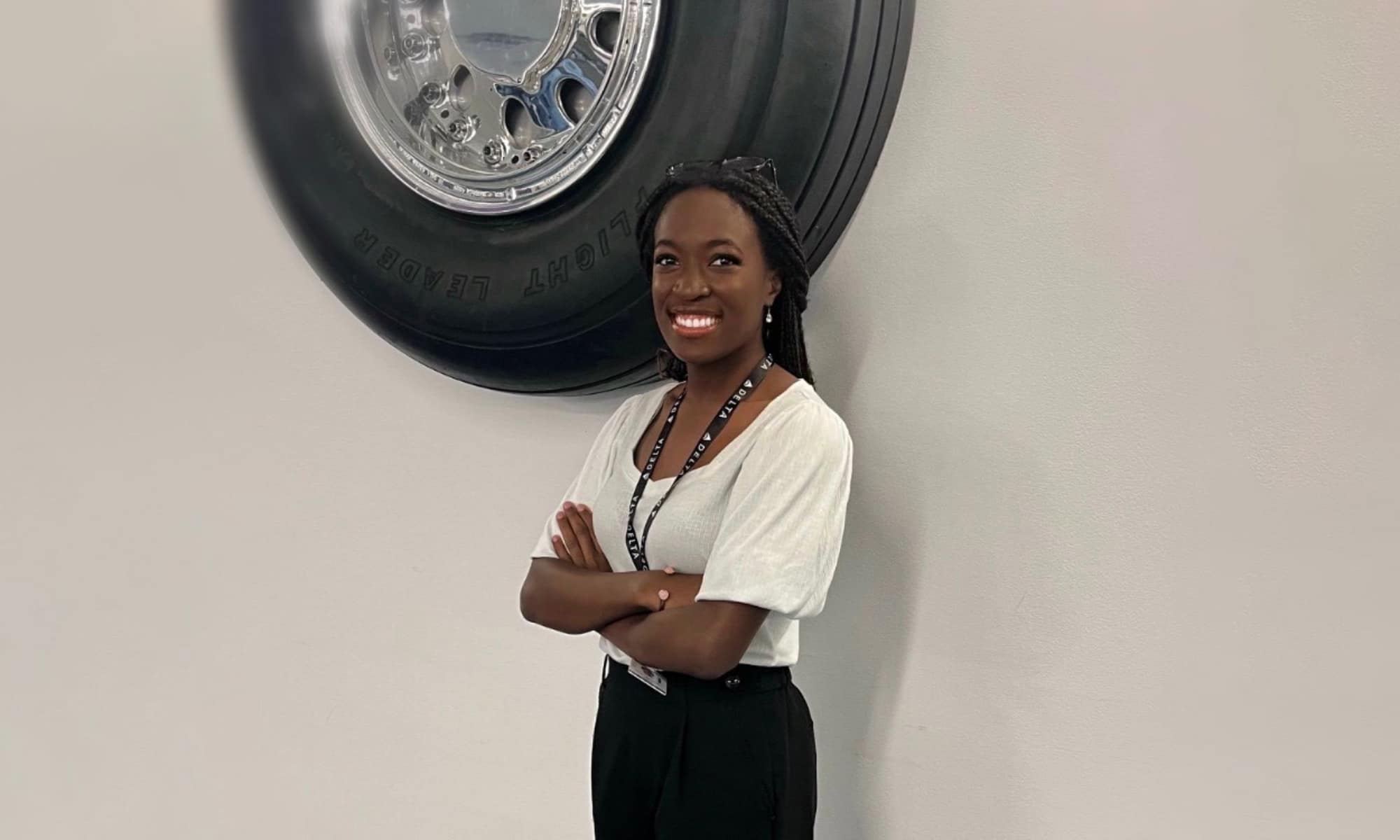 Faith, wearing a white blouse and a lanyard, poses in front of an illustration of a tire.
