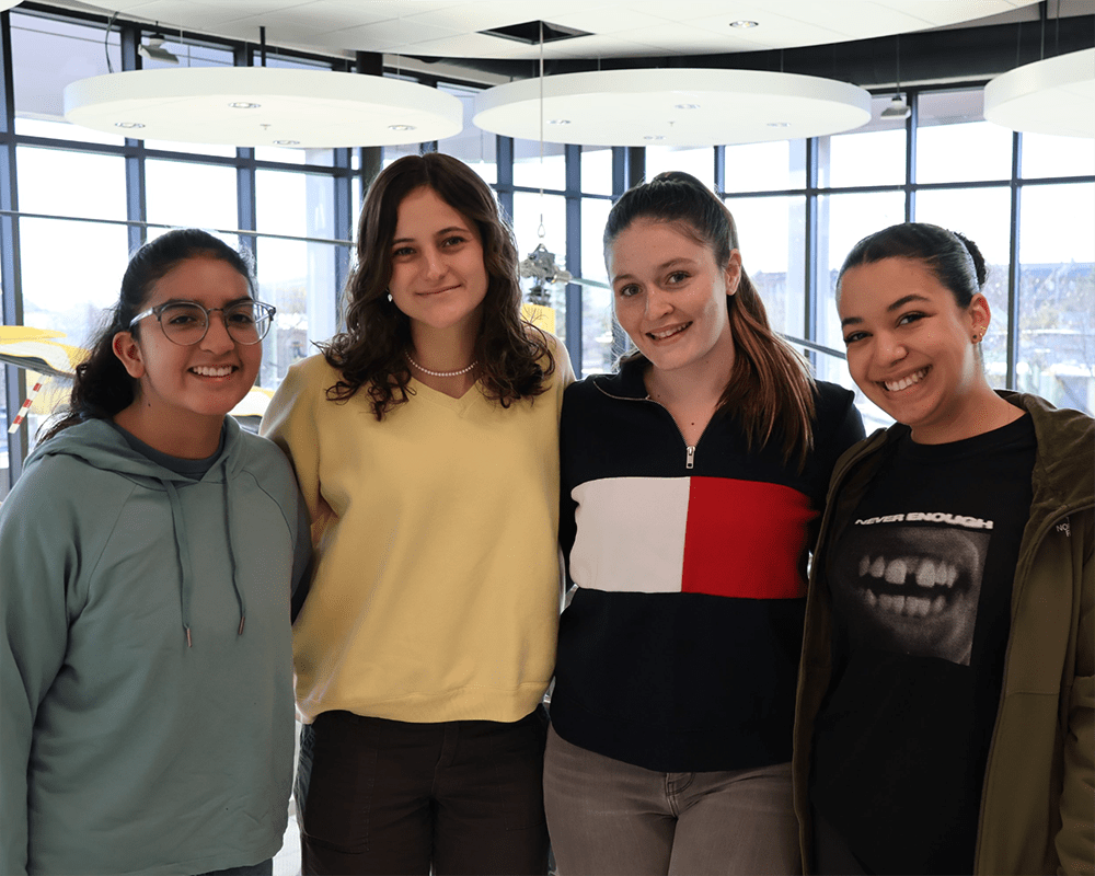 Makenzi poses with three friends in front of a wall of windows.