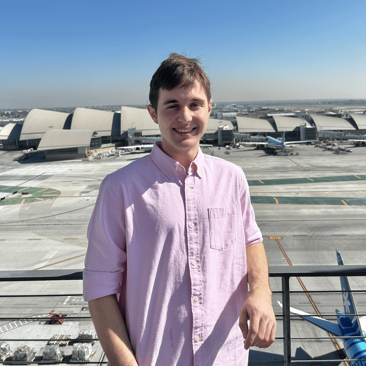 Timothy, smiling in a pink button down shirt, with the LAX terminal behind him.