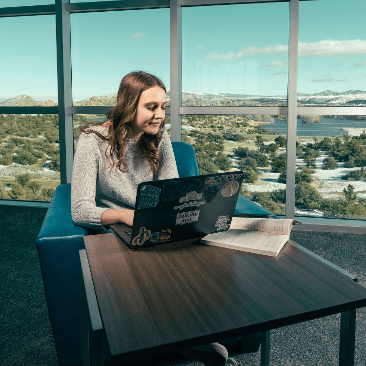 A student studies in front of large windows.