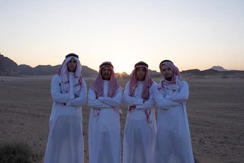 Four men dressed in thobes standing in a desert landscape