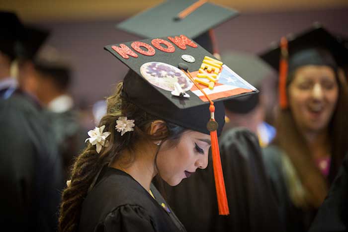 A woman stands at graduation, wearing a cap with a flag of Puerto Rico and the words "Moon" and "Next" 
