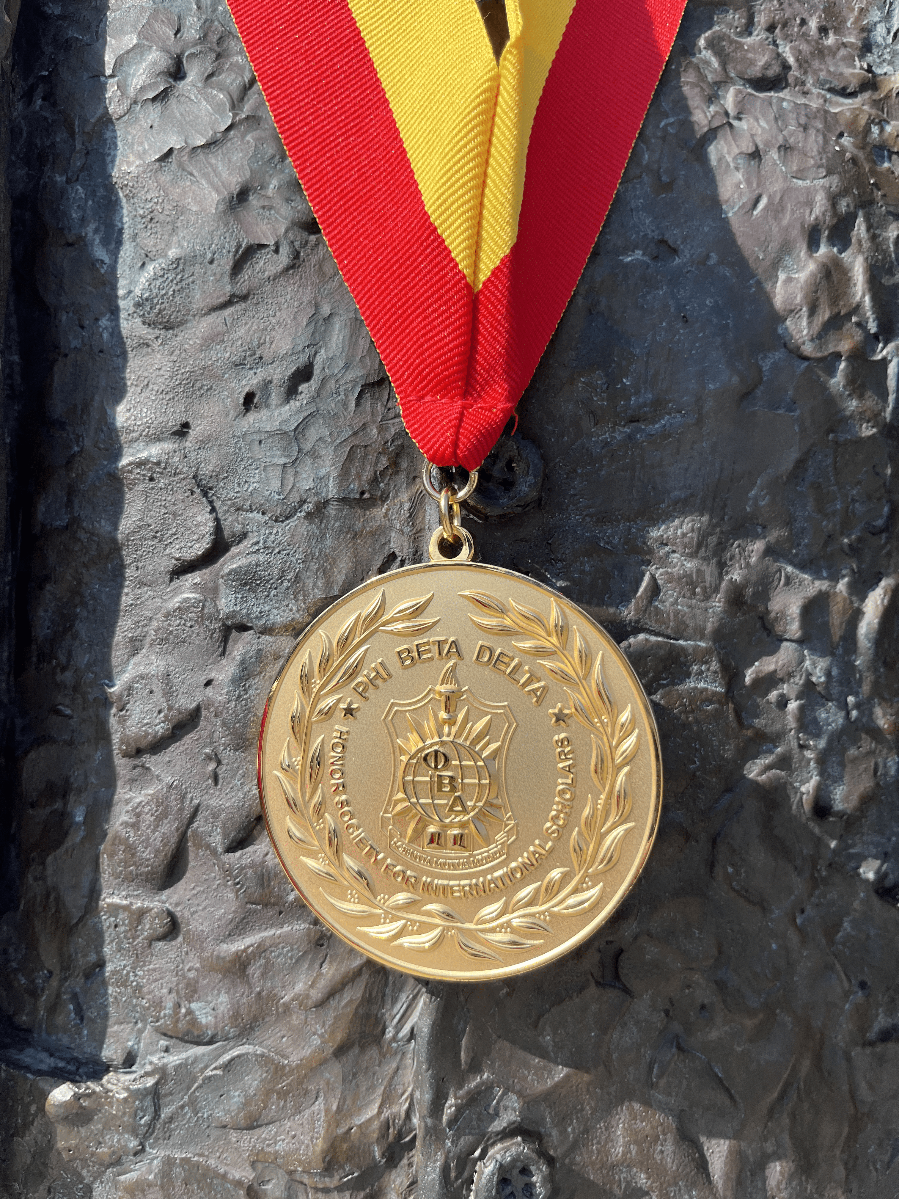 A gold circular medal hanging from a red and yellow ribbon.