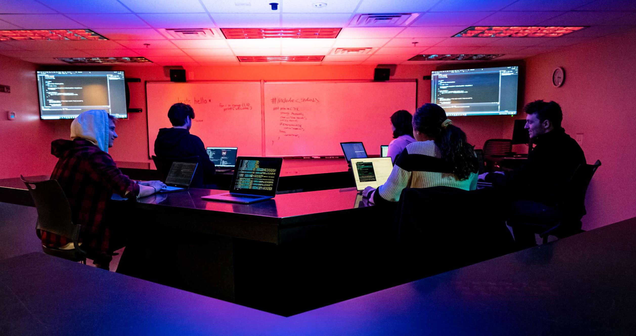 A group of cybersecurity students study code in a dynamic classroom setting.