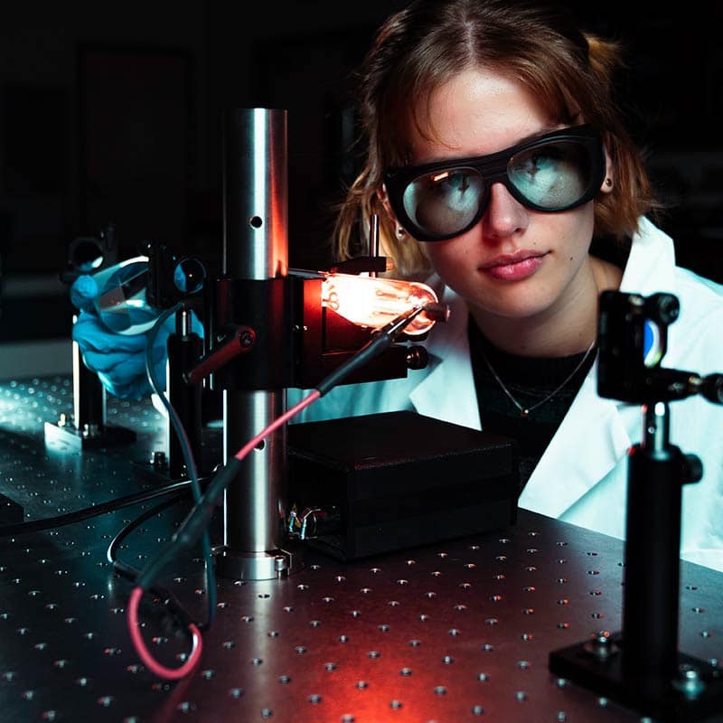 Young woman conducts tests with optical equipment in lab.