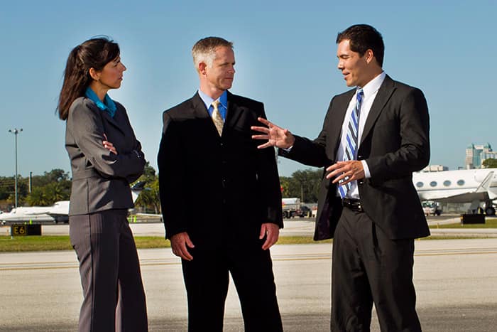 a woman and two men talk on an airport tarmac